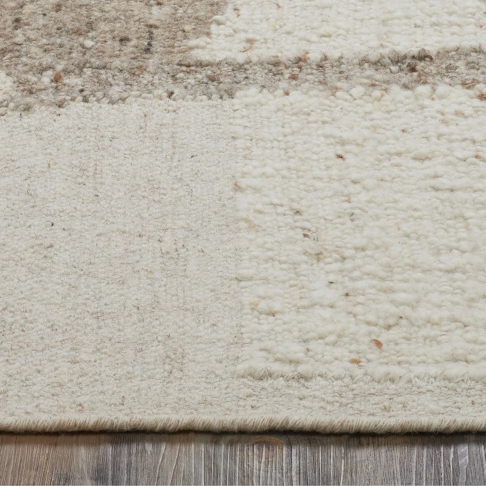 Close-up of a textured beige rug with subtle patterns on a wooden floor.
