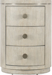 A beige round nightstand with three drawers and circular knobs on each drawer.