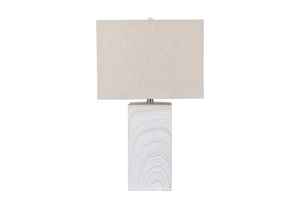 A transitional style table lamp with a beige shade and a white ceramic base with a channelled pattern.