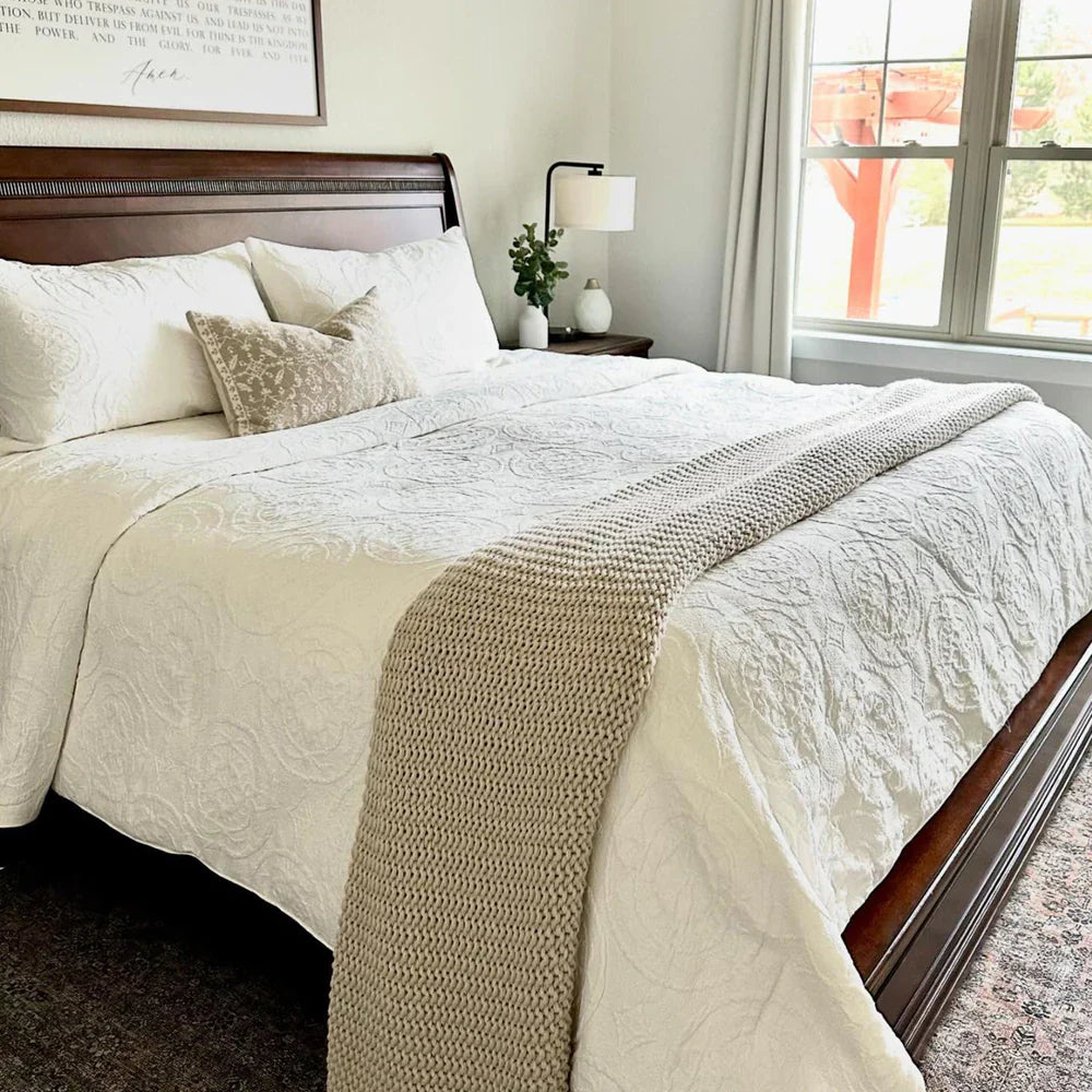 Neatly made bed with beige and white bedding in a well-lit bedroom.