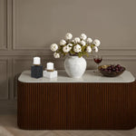 Decorative table with a vase of flowers, candles, and fruit against a wall.