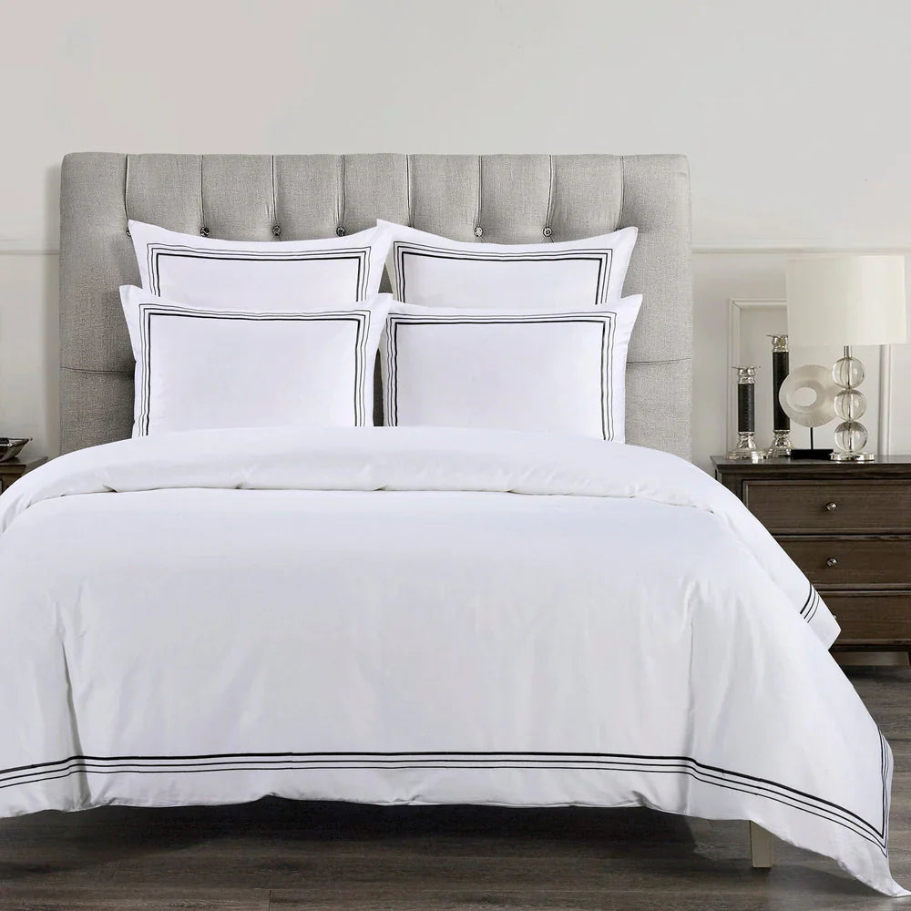 White bedding set with black trim on a bed with a gray upholstered headboard.