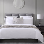 Neatly made bed with white bedding and gray pillows in a bedroom setting.