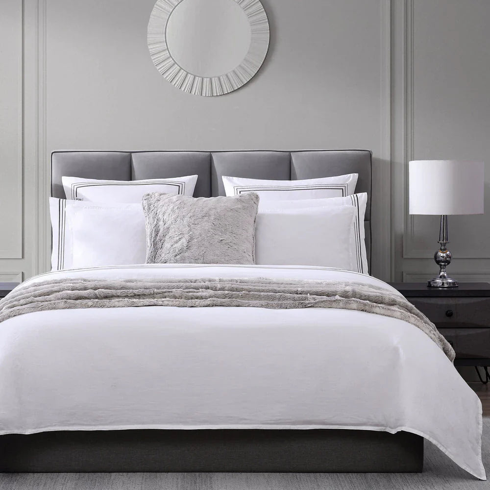 Neatly made bed with white bedding and gray pillows in a bedroom setting.