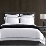 White bedding set with black trim on a bed against a wooden wall.