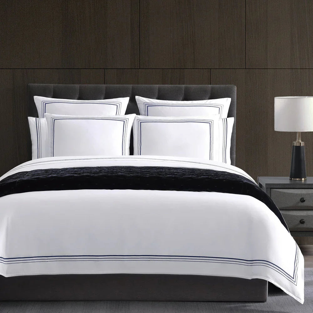 White bedding set with black trim on a bed against a wooden wall.