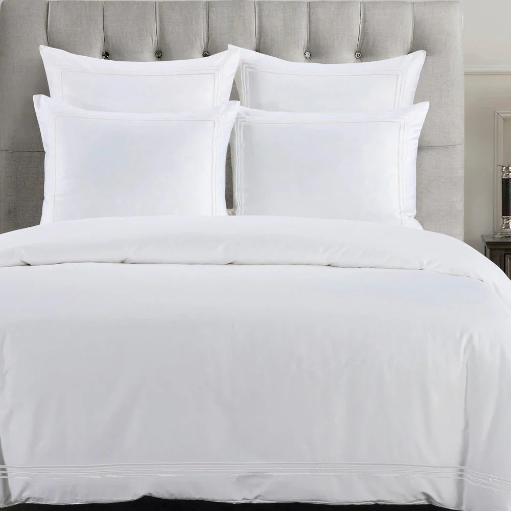 White bedding set on a bed with a gray upholstered headboard.