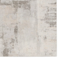 A white area rug with a geometric pattern featuring various shades of grey and a subtle wood floor appearance.