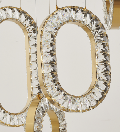 A gold-colored LED chandelier with a modern design, featuring circular and oval shapes with crystal accents, suspended by adjustable cords.