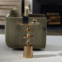 Gold side table with a cup of coffee next to a green armchair in a room.