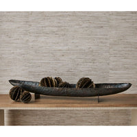 Decorative metal bowl with spherical elements on a wooden surface against a textured wall.