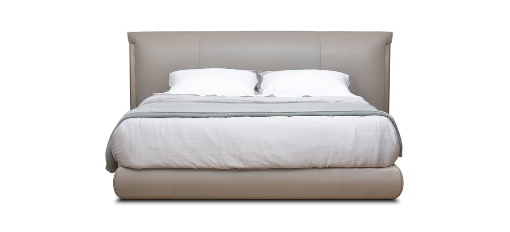 A beige upholstered headboard on a bed with white sheets.