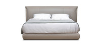 A beige upholstered headboard on a bed with white sheets.