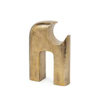 Gold metal sculpture of interlocking shapes on a white background