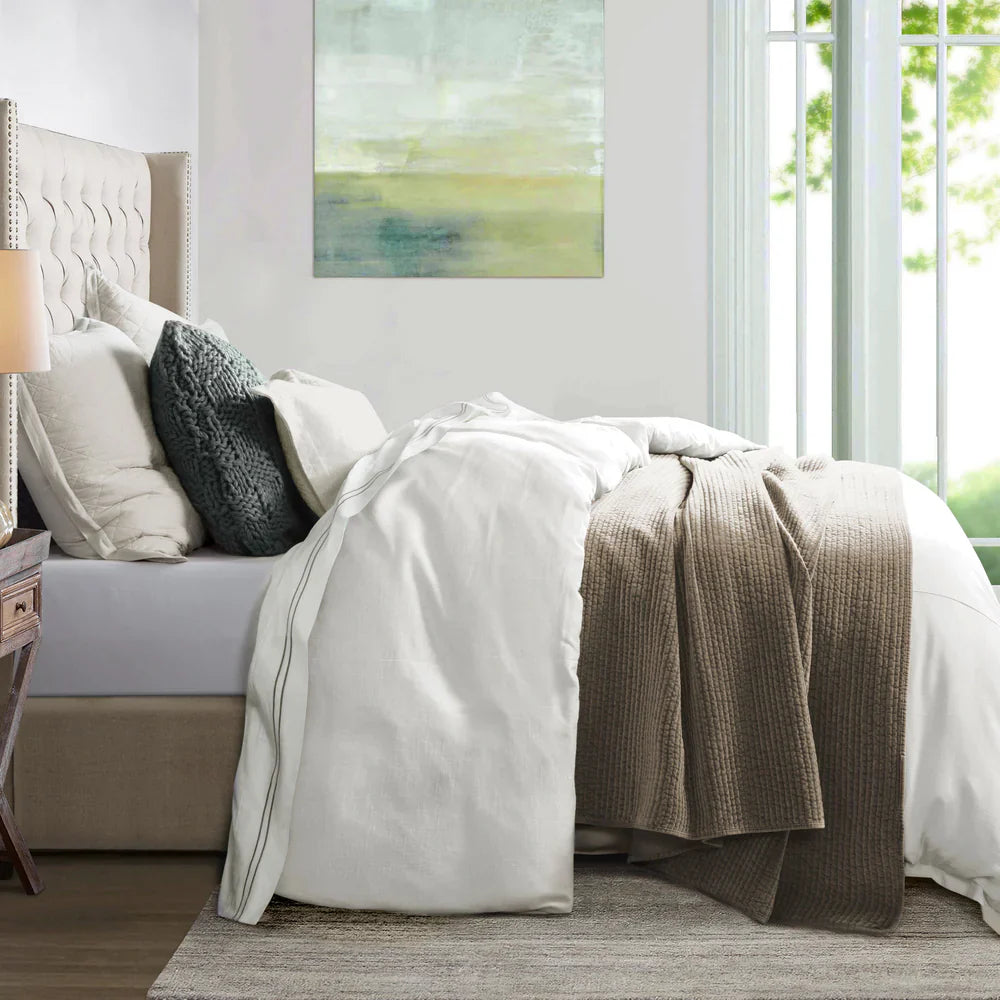 Neatly made bed with beige and white bedding in a bright bedroom.
