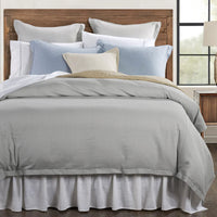 Bed with gray comforter, colorful pillows, and wooden headboard in a room with a window.