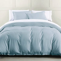 Blue bedding set on a bed with white pillows against a light-colored wall.