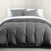 Gray bedding set on a bed with white pillows against a neutral wall.