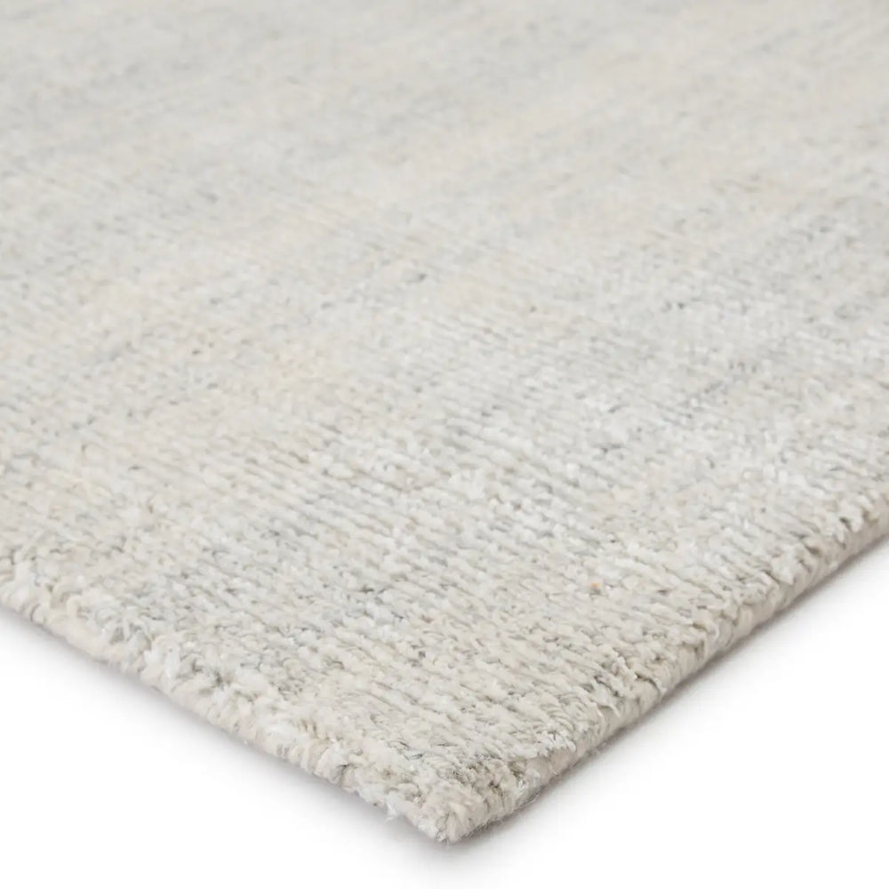 An ivory-colored area rug with a textured weave, partially showing its thickness and material.