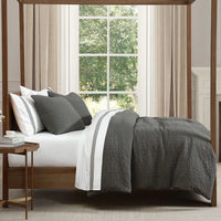 Bedroom with a canopy bed featuring gray bedding and pillows, next to a window with white curtains.