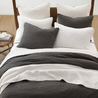 Bed with gray and white bedding and pillows in a bedroom setting.