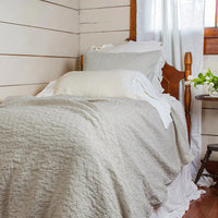 Bed with gray bedding and white pillows in a room with wooden walls and a window.
