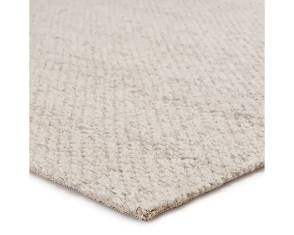 A beige, solid color wool area rug handwoven with a visible texture.