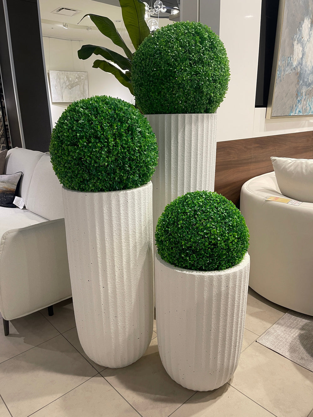 A set of three white, textured planters with stripes, each holding a green spherical plant.