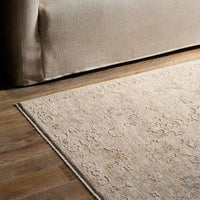 Beige rug on a wooden floor next to a beige sofa.