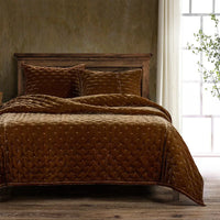 Brown quilted bedding set on a bed with a wooden headboard in a room with a window and plant.