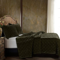 Bed with green textured bedding against a textured wall.