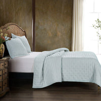 Bed with light blue quilt and pillows in a bedroom setting